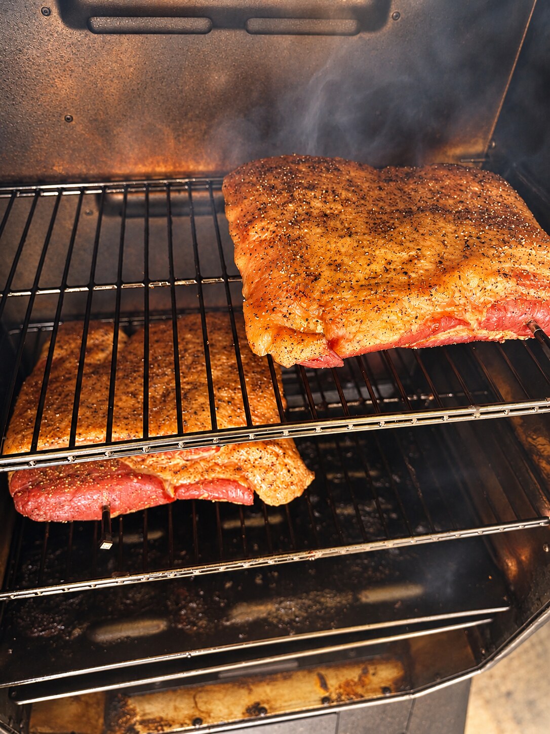 Peppered bacon slabs smoking over hardwood